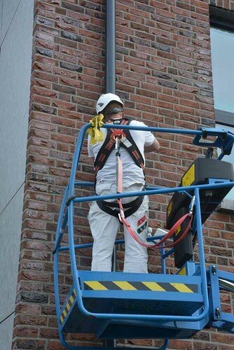 Photo showing a worker carrying out maintenance work on a rain pipe who has hooked up his safety harness for added fall protection