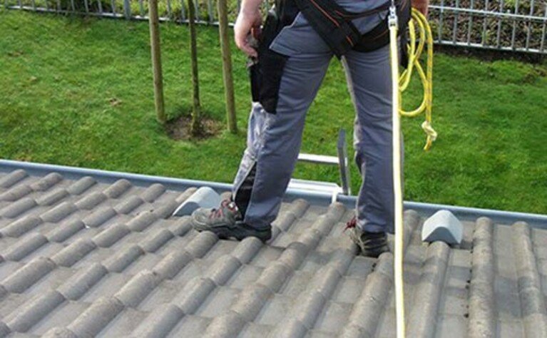 Foto eines Dacharbeiters, der sich an einer Anschlagschlaufe angeleint vor einem Absturz schützt.