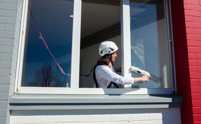 Das Bild zeigt eine angeleinte Frau, die ein Fenster reinigt und sich dazu hinauslehnt.