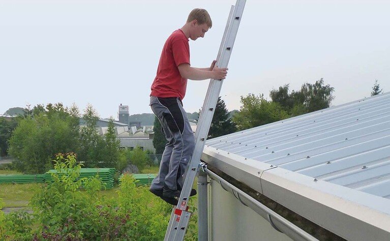 Een dakwerker stapt van de beveiligde ladder op het dak.