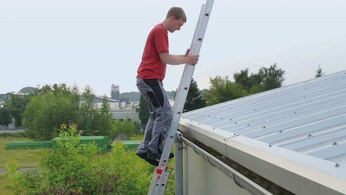 Einsatzfoto eines Dacharbeiters, der vom oberen Ende einer gesicherten Leiter aufs Dach steigt.