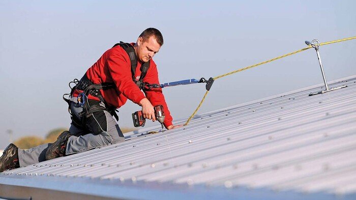 Image showing an installation technician working on a sandwich roof surface who has connected up to an anchor to protect himself from falling